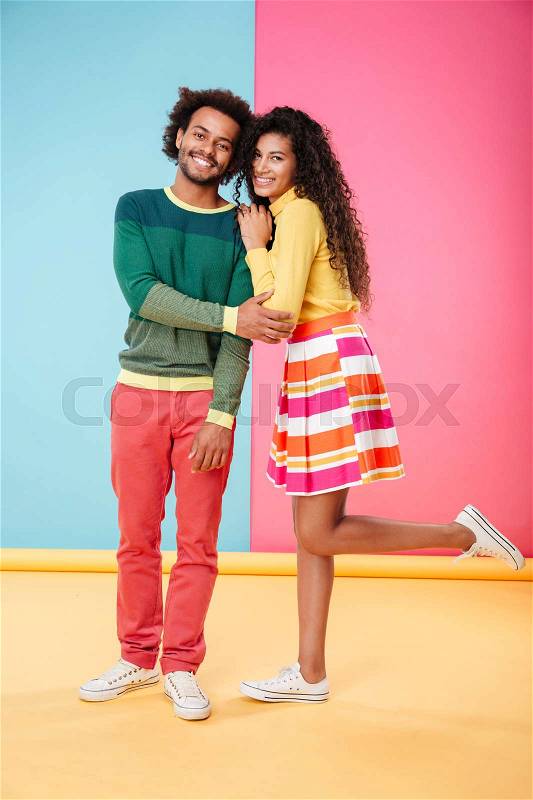 Portrait of smiling african young couple in clothes standing together over colorful background, stock photo