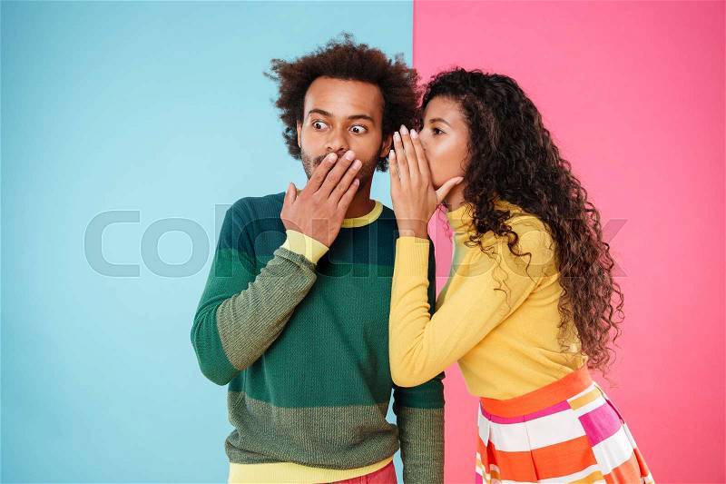 Beautiful curly young woman telling secrets to her boyfriend over colorful background, stock photo