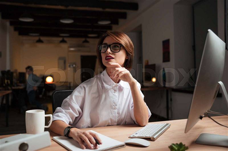 Happy pensive young businesswoman in glasses thinking and working in office, stock photo
