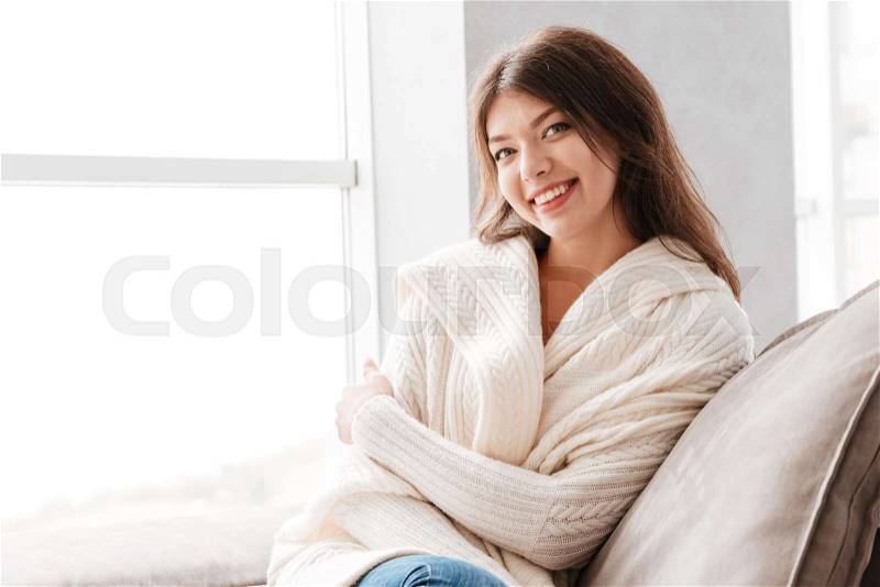 Portrait of happy beautiful young woman sitting on couch at home, stock photo