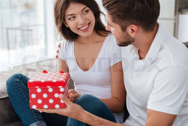Cheerful young woman taking present from her boyfriend at home, stock photo