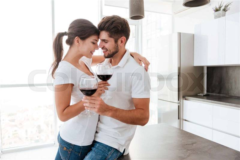 Happy sensual young couple hugging and drinking red wine on the kitchen, stock photo