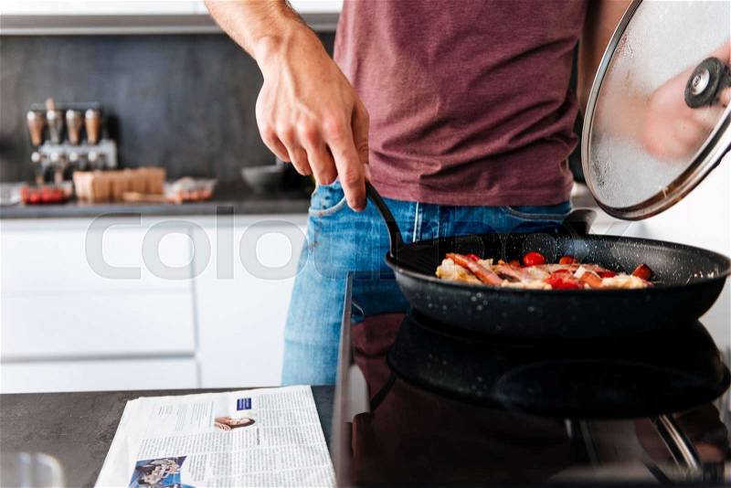 Closeup of man standing and using frying pan on the kitchen, stock photo