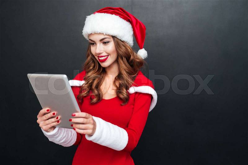 Smiling young woman in red christmas costume using tablet over black background, stock photo