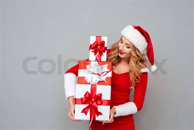 Attractive blonde woman standing with heap of gift boxes isolated on the gray background, stock photo