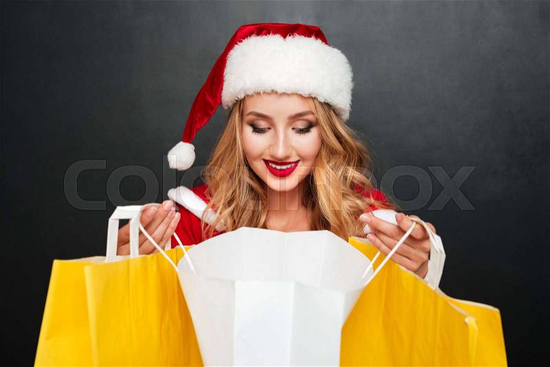 Cheerful woman in santa claus costume looking inside shopping bag, stock photo