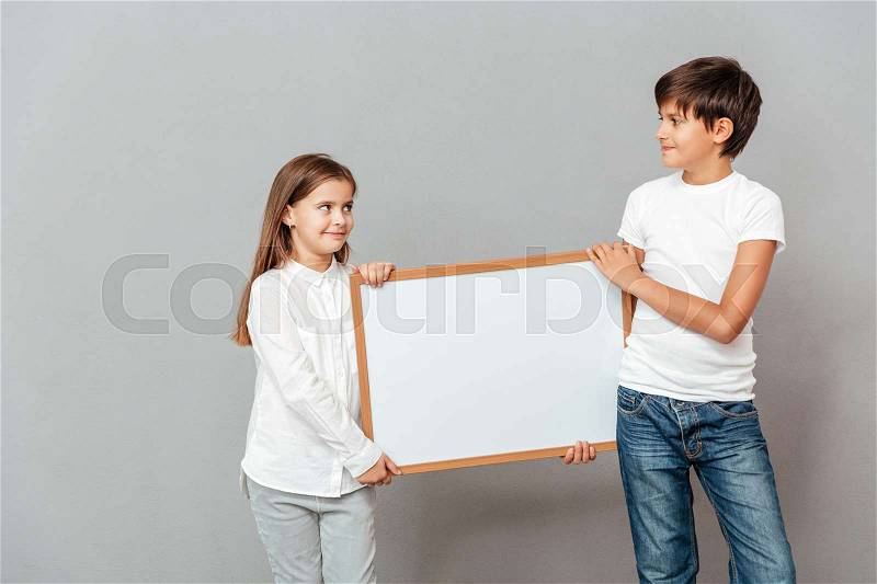 Happy little boy and girl holding blank white board together, stock photo