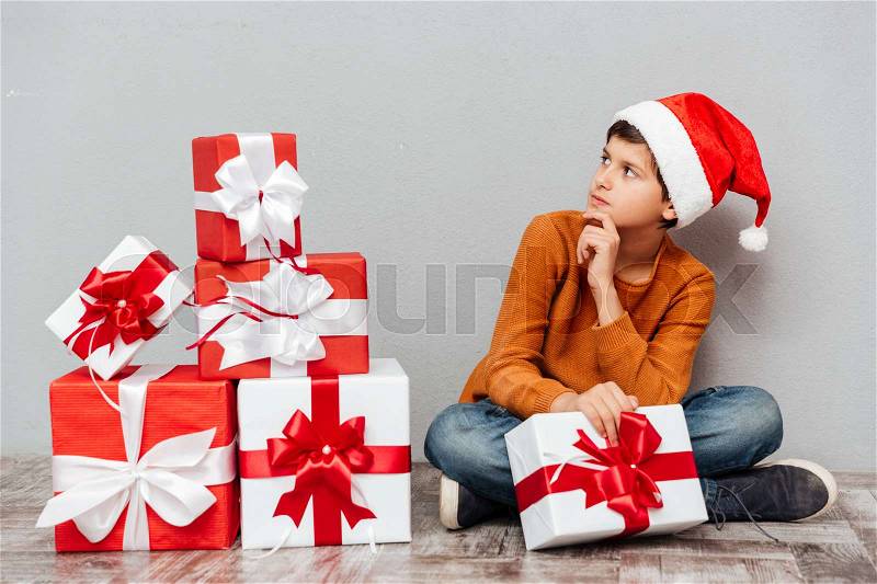 Thoughtful boy in santa claus hat with gift box sitting and looking away, stock photo