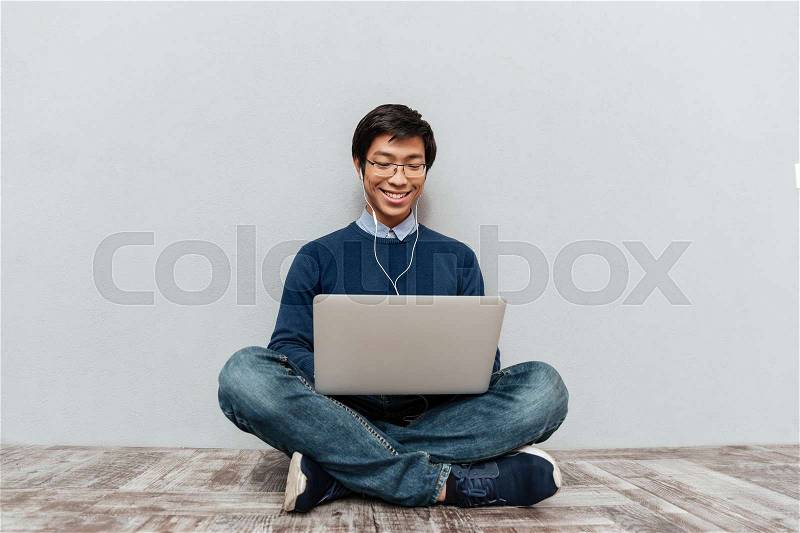 Asian man with laptop sitting on the floor. smiling model, stock photo