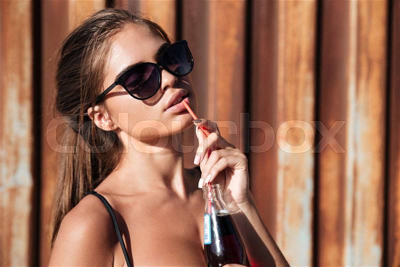 Woman in sunglasses drinking soda over rusty metal background, stock photo