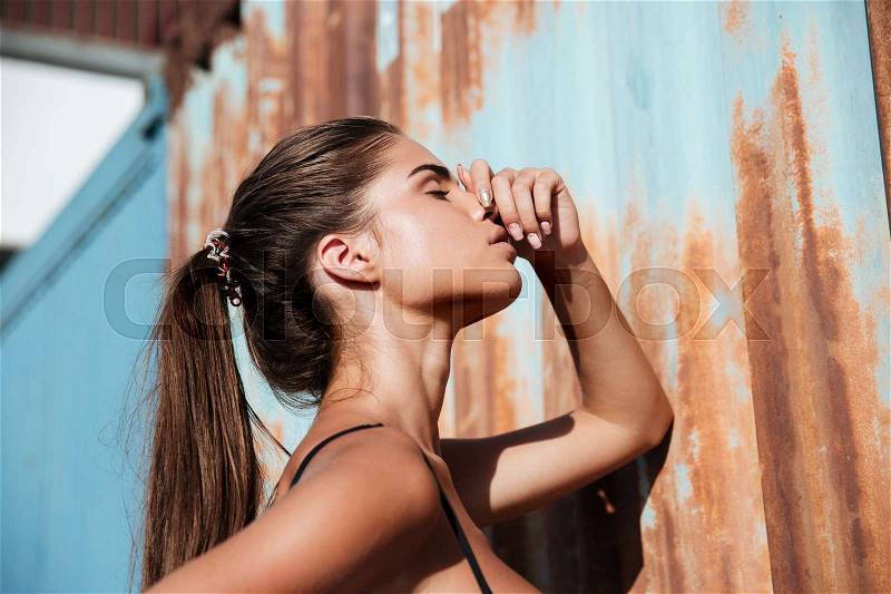 Sensual young woman with ponytail standing and touching her nose, stock photo
