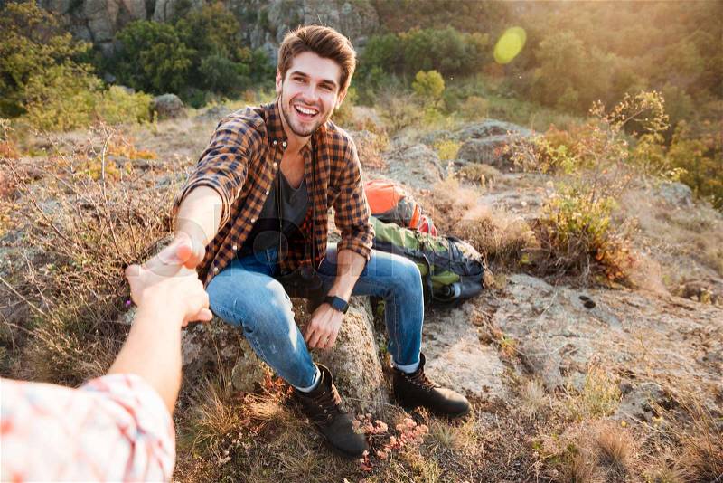 Young woman helps her boyfriend to get up on their hiking journey, stock photo