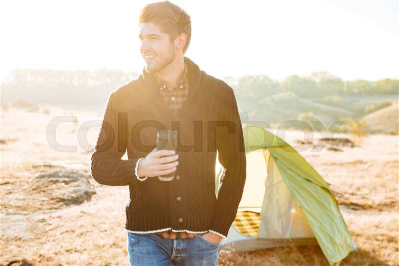 Young happy man drinking coffee outdoors with tent on the background, stock photo
