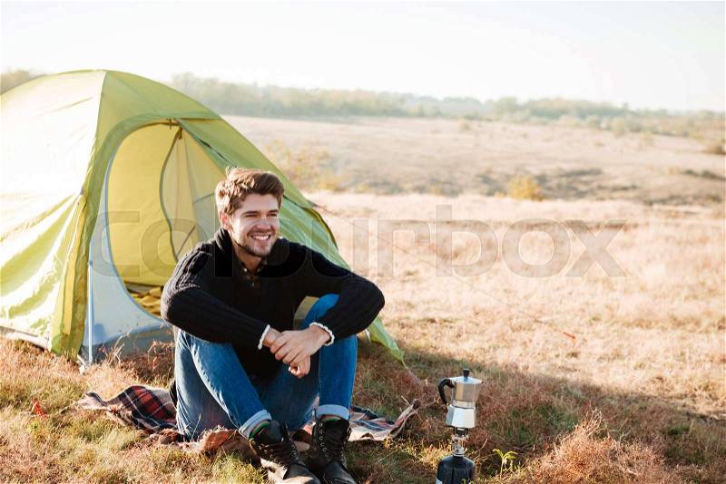 Young happy man sitting outdoors with tent on the background, stock photo