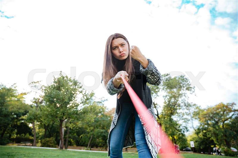 Angry strict young woman showing fist to her dog in park, stock photo