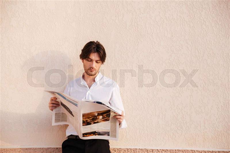 Serious young businessman reading newspaper. on pink background. standing near the wall, stock photo