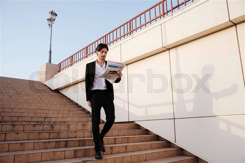 Man in suit with newspaper walking on stairs. so cool model, stock photo