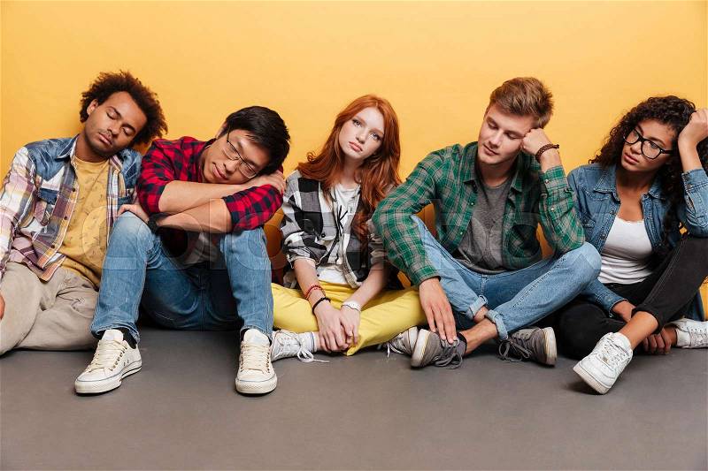 Group of tired young people sitting and sleeping over yellow background, stock photo