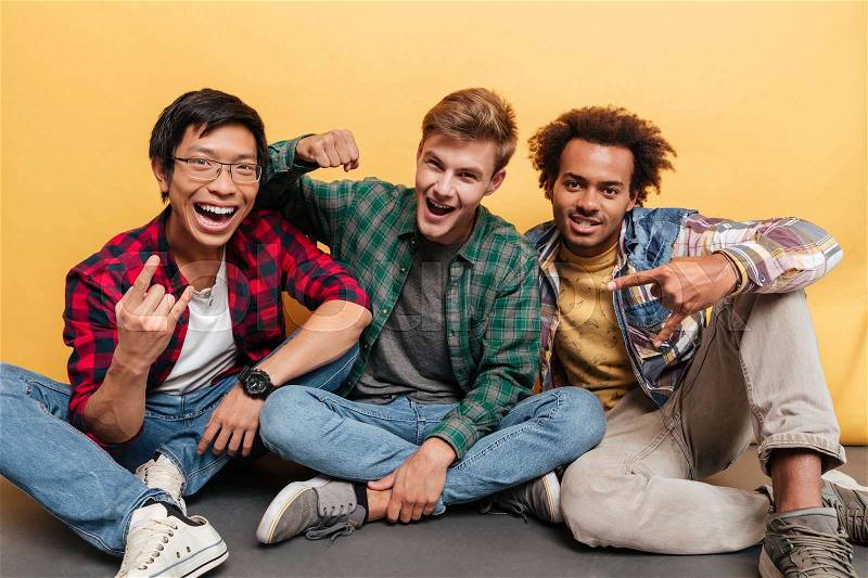 Three cheerful young men friends shouting and celebrating success over yellow background, stock photo