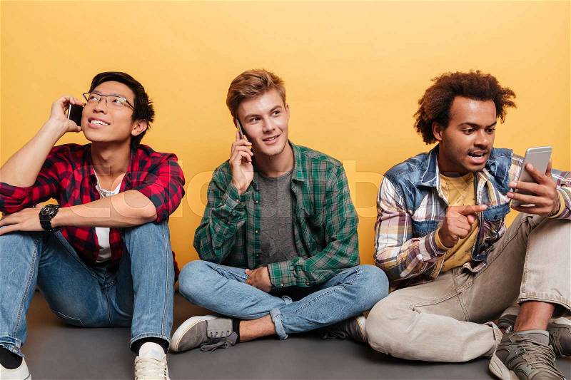 Three young men friends talking on mobile phone over yellow background, stock photo