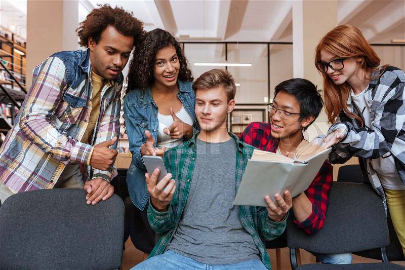 Handsome young man reading and using mobile phone while his friends standing around him, stock photo