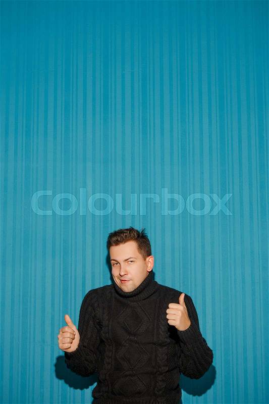 Portrait of young man with serious facial expression showing OK over blue studio background, stock photo