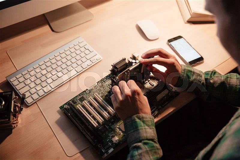 Concentrated young man sitting and repairing motherboard in the dark room, stock photo