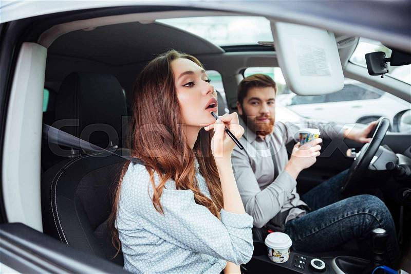 Beauty couple in car with coffee. man the wheel looking at girl. girl paints her lips. side view, stock photo