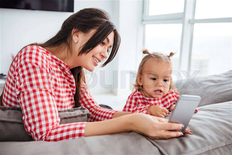 Happy mother and her cute daughter are looking at mobile. in dresses. on bed, stock photo