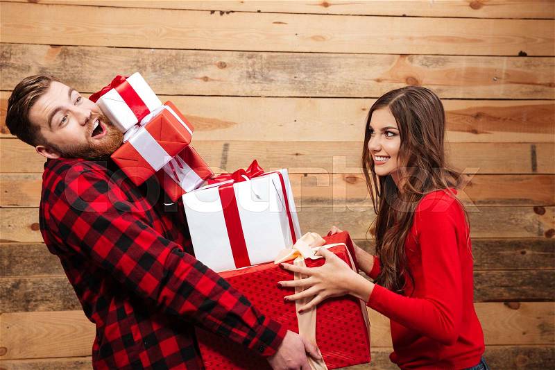 Happy funny couple standing with heap of xmas present boxes isolated on a wooden background, stock photo
