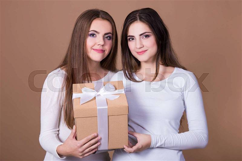 Holidays and friendship concept - two girls with gift box over beige background, stock photo