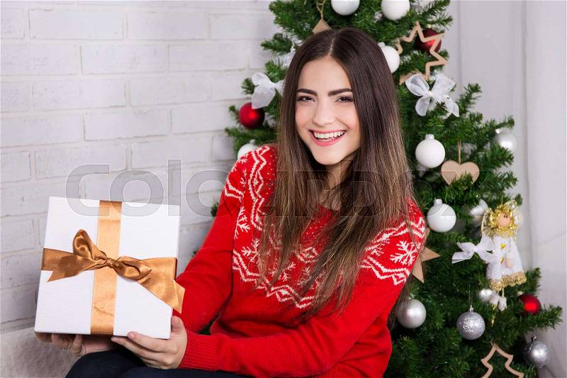 Young laughing woman opening gift box near decorated christmas tree, stock photo