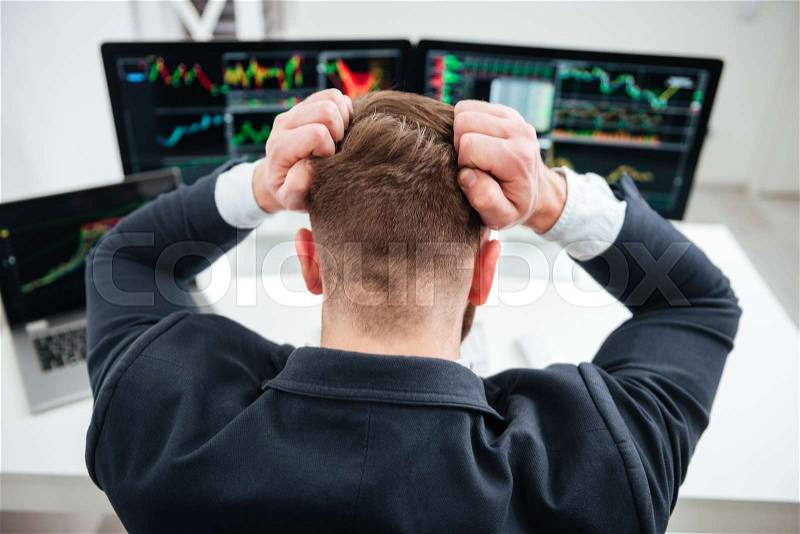 Back view of stressed irritated businessman sitting and working with computer in office, stock photo