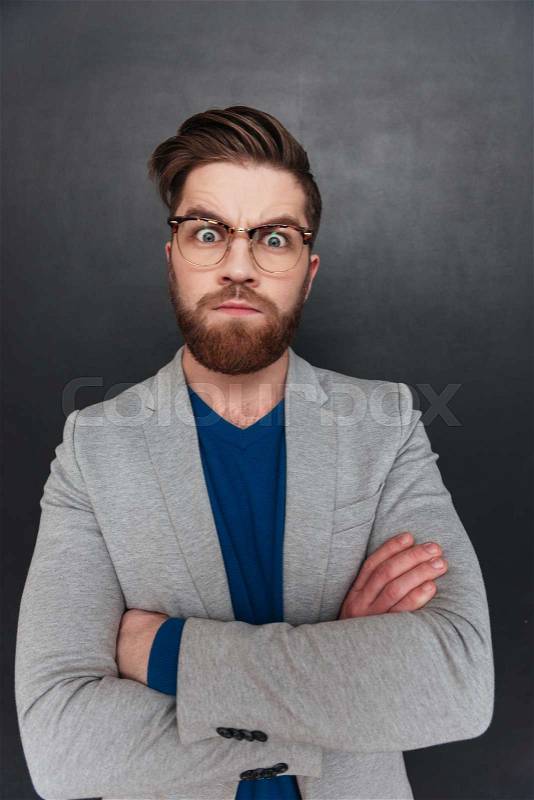 Angry serious young businessman in glasses standing with arms crossed, stock photo