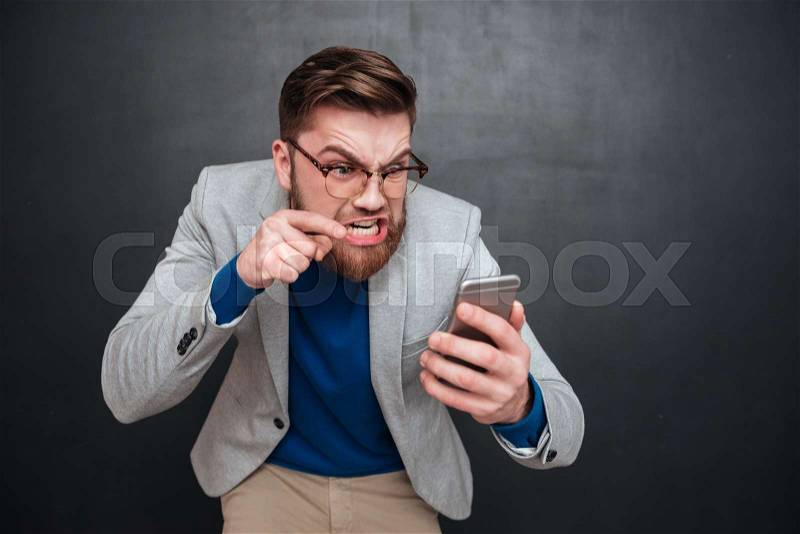 Irritated guy with phone in studio. hipster. isolated black background, stock photo