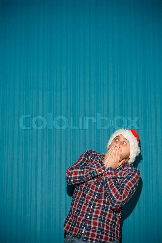 The frightened christmas man wearing a santa hat on the blue studio background pointing up, stock photo