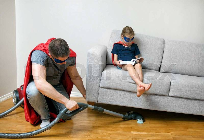 Ordinary day of superhero family. Dad vacuuming, daughter reading a book, stock photo