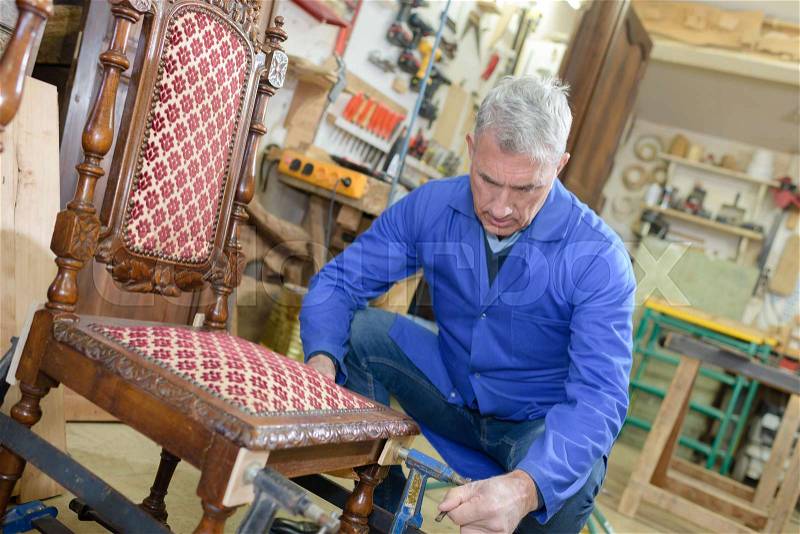 Old craftsman repairing a chair in his workshop, stock photo