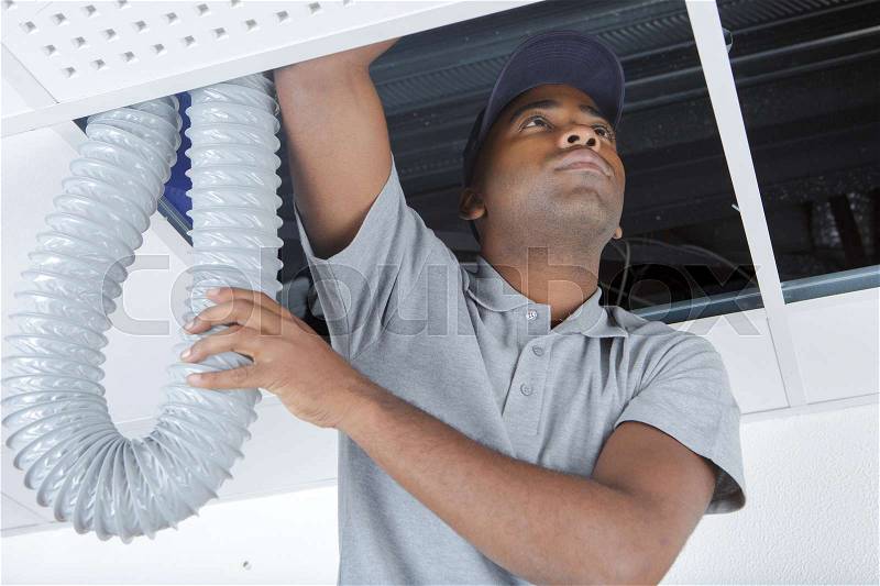 Young male electrician on stepladder installing pipes in ceiling, stock photo