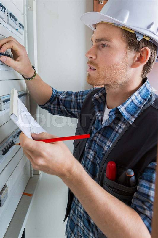 Young electrician working on electric panel, stock photo