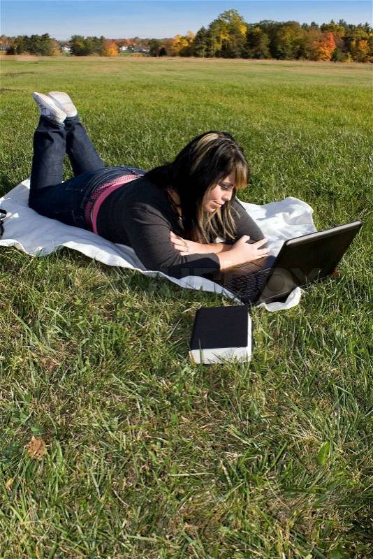 A young student using her laptop computer while laying in the grass on a nice day, stock photo