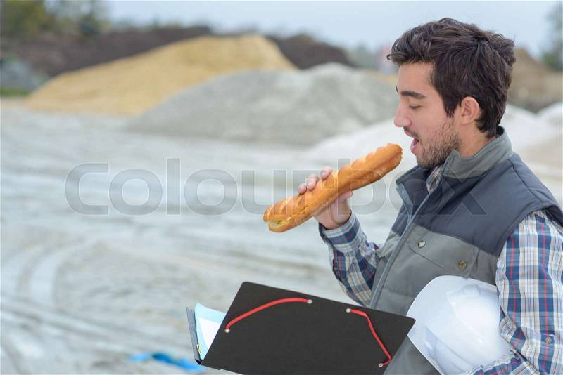 Man eating baguette on building site, stock photo