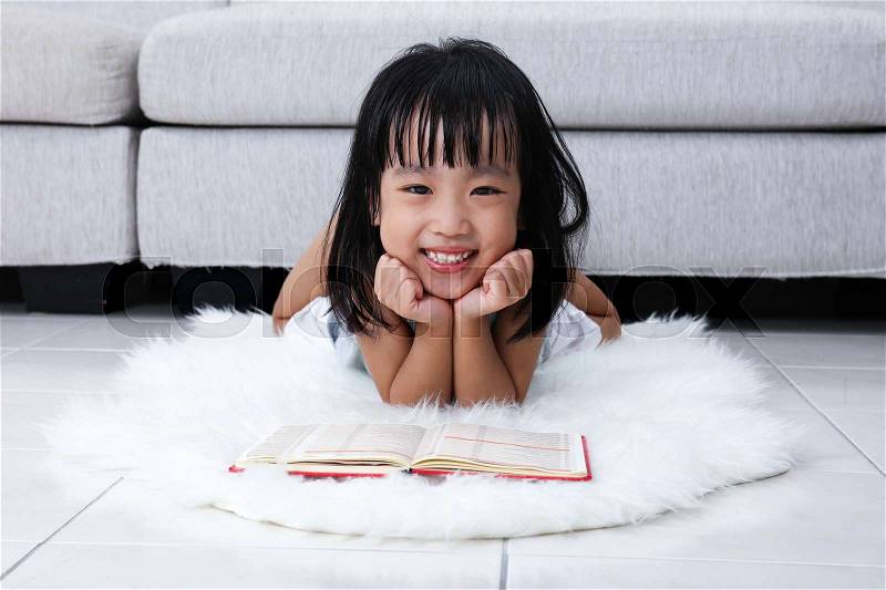 Happy Asian Chinese little girl reading book on the floor in the living room at home, stock photo