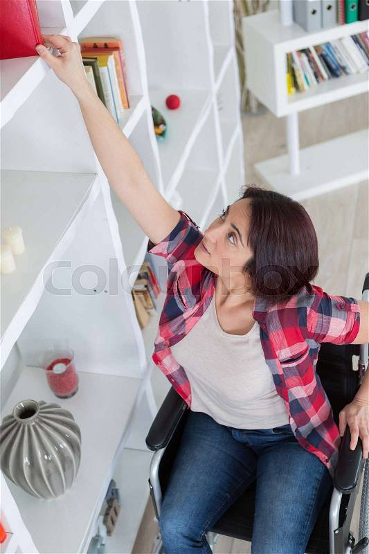 Young disabled woman reaching out for blanket at shelf, stock photo