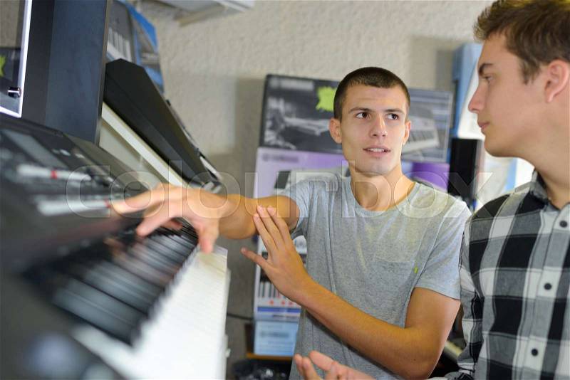 Happy young man trying a piano at music store, stock photo