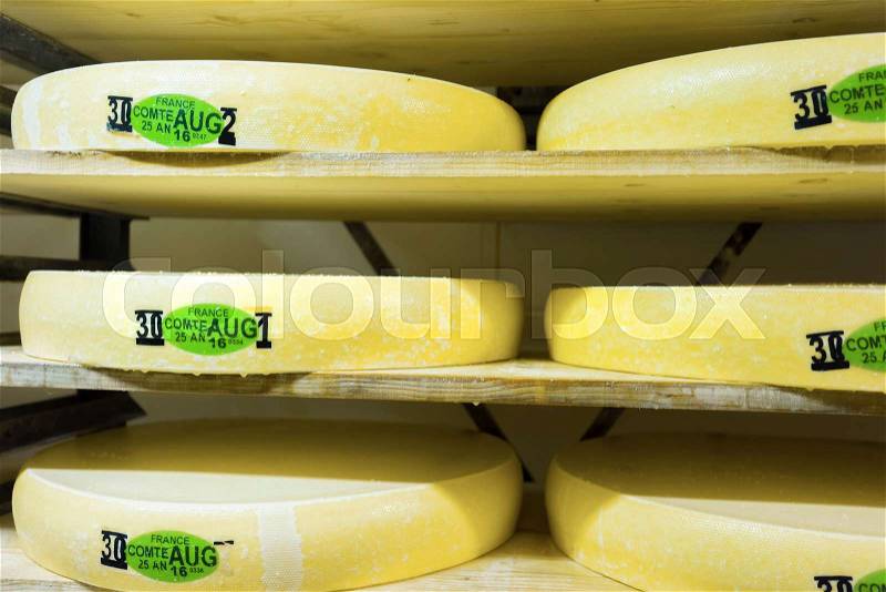 Stack of aging Gruyere de Comte Cheese on wooden shelves in ripening cellar of Franche Comte creamery in France. It is written - France, Comte, August 25, 2016, stock photo