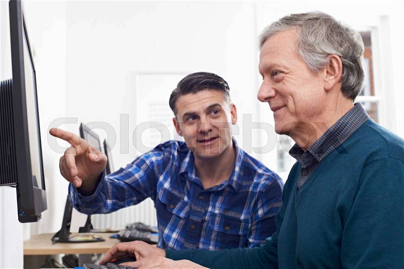Tutor Helping Mature Man In Computer Class, stock photo