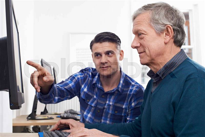Tutor Helping Mature Man In Computer Class, stock photo