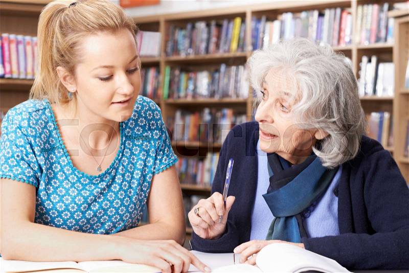 Senior Woman Working With Teacher In Library, stock photo