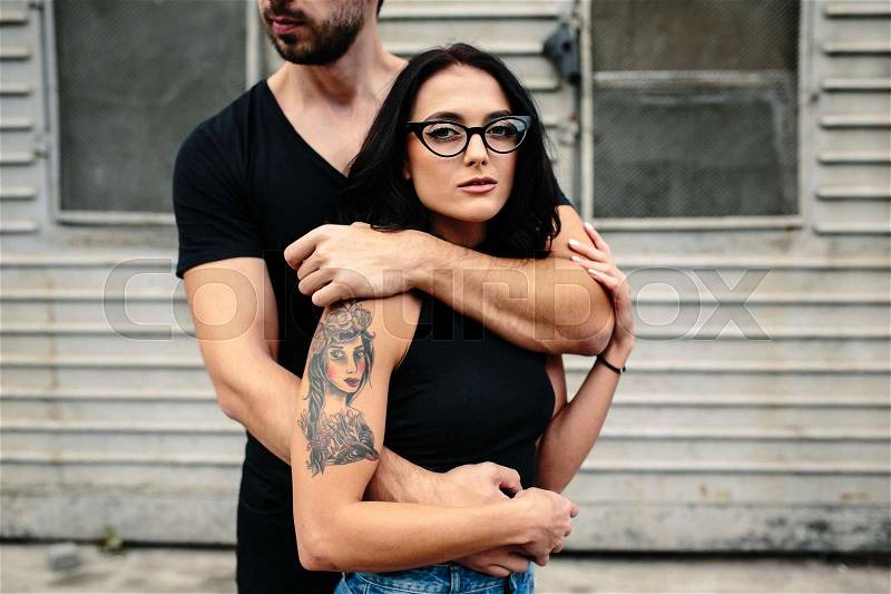 Guy hugging his girlfriend from behind against a background of gray wall, stock photo